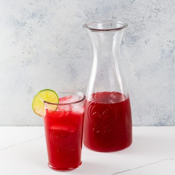 raspberry limeade in a carafe and in a glass garnished with a lime wheel