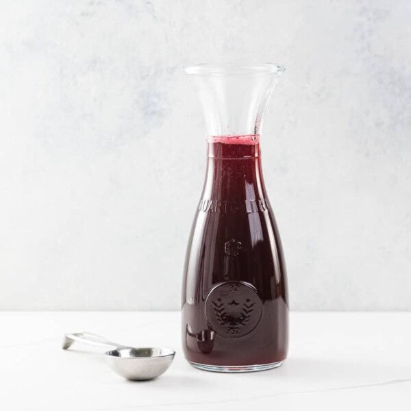 raspberry simple syrup in a small carafe with a measuring spoon
