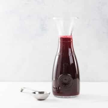 raspberry simple syrup in a small carafe with a measuring spoon