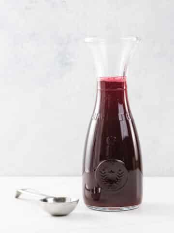 raspberry simple syrup in a small carafe with a measuring spoon