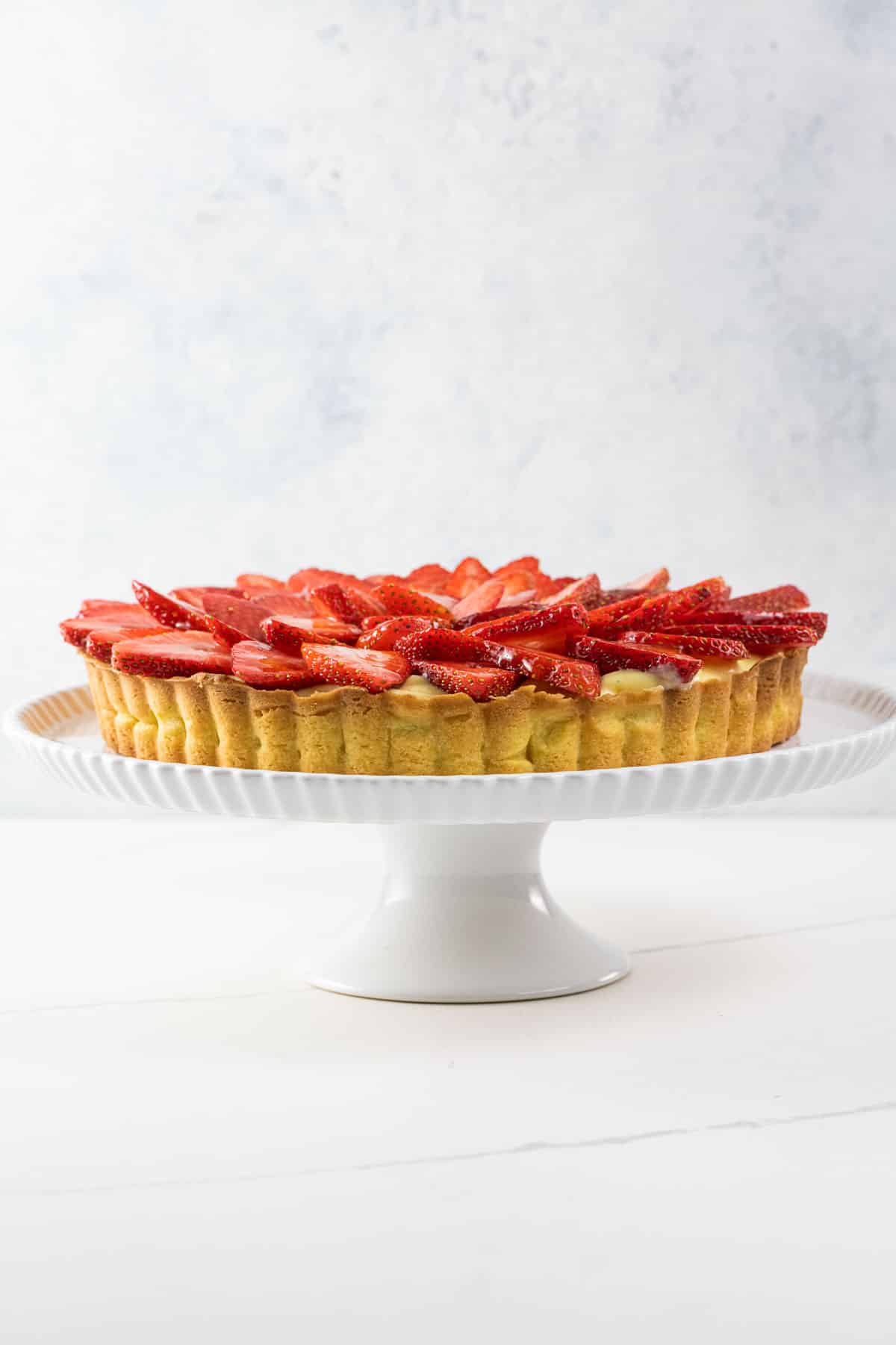 a strawberry custard tart on a cake stand