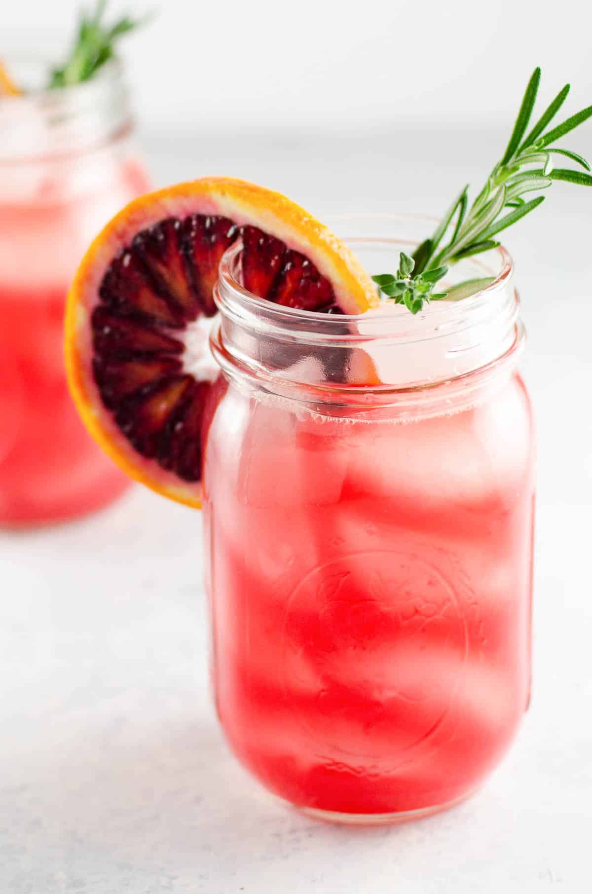 a blood orange cocktail in a mason jar garnished with a rosemary sprig and a blood orange wheel