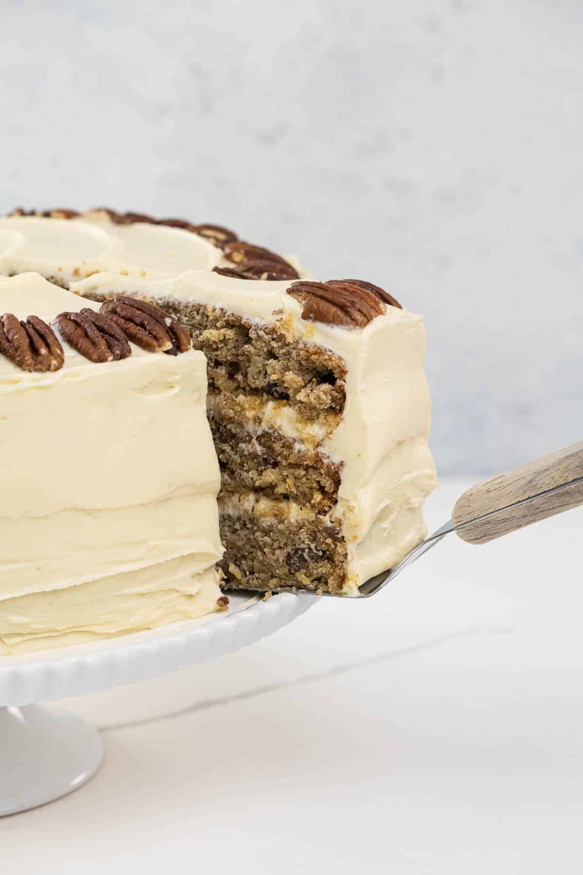 an old fashioned hummingbird cake on a cake stand with a slice being removed