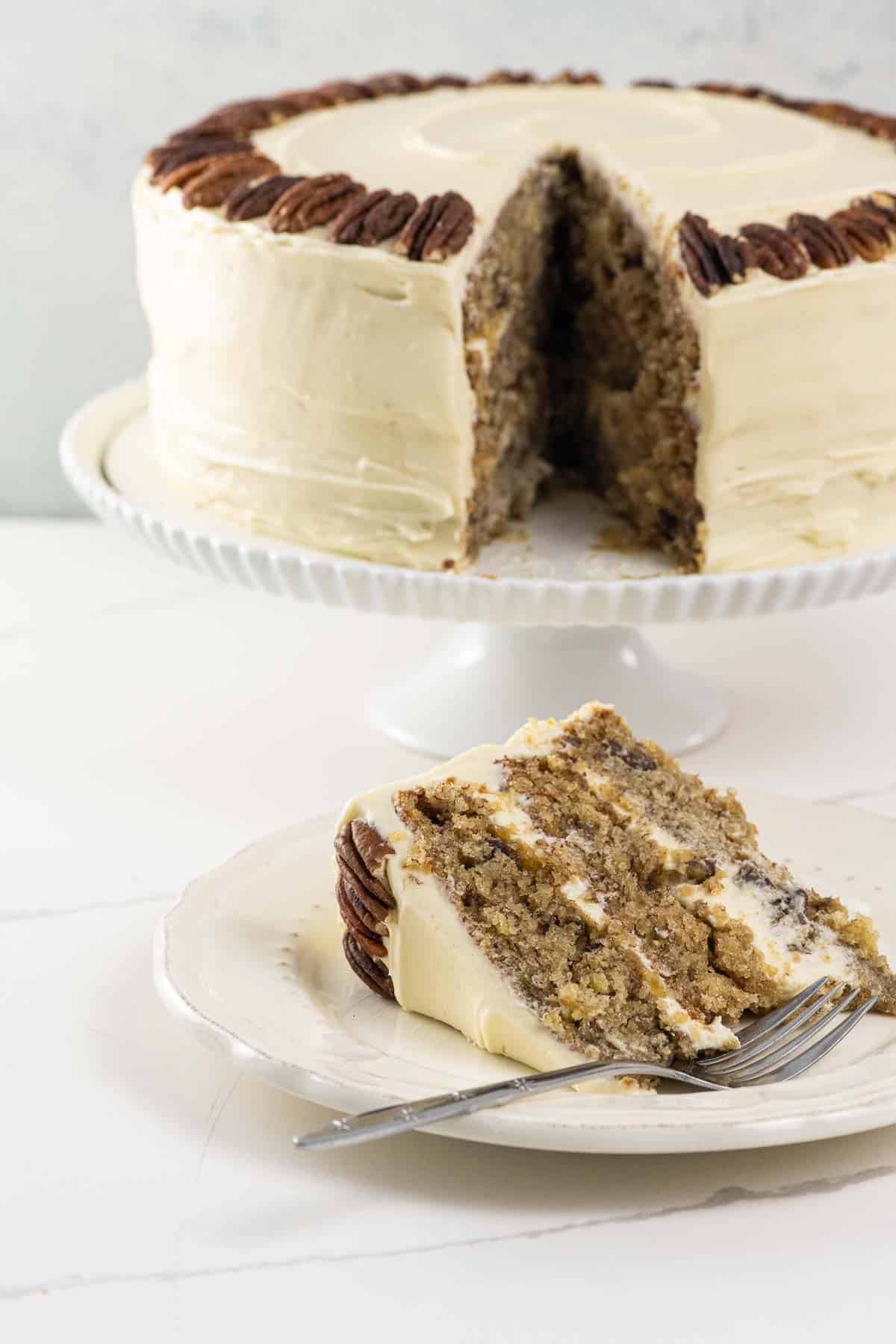 an old fashioned hummingbird cake on a cake stand with a slice on a plate with a fork