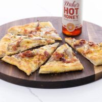 pear gorgonzola pizza with prosciutto and hot honey on a cutting board with a bottle of hot honey