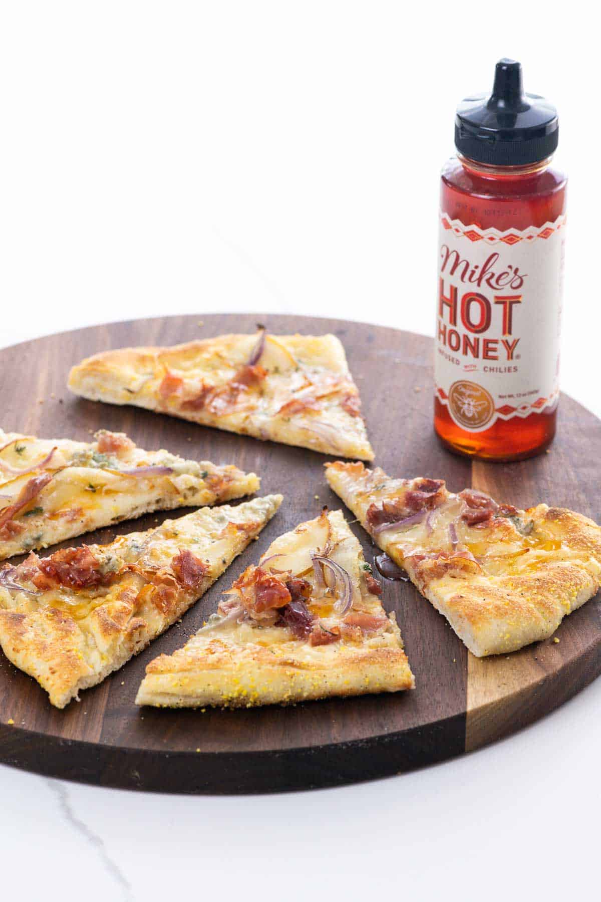 pear gorgonzola pizza with prosciutto and hot honey on a cutting board with a bottle of hot honey