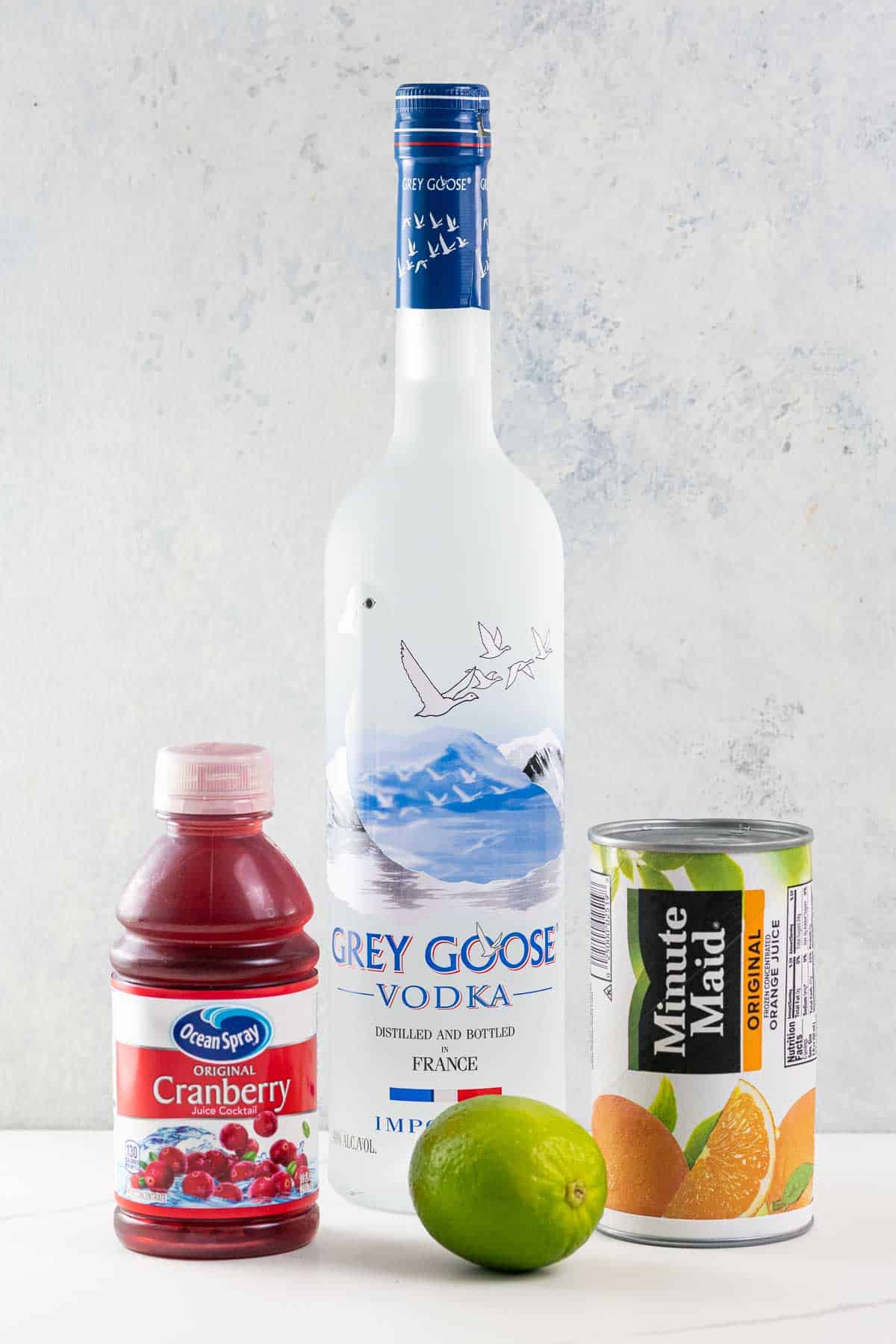 a bottle of grey goose vodka, a small bottle of ocean spray cranberry juice cocktail, a lime, and a can of minute maid orange juice concentrate