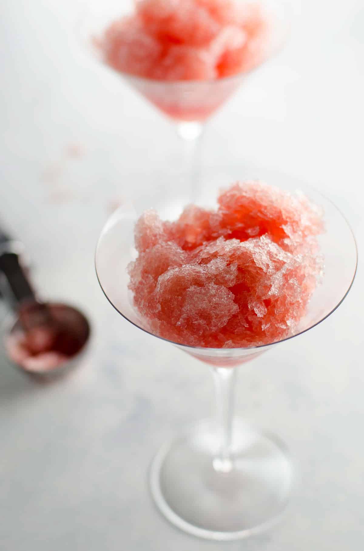 two martini glasses filled with the red rooster frozen vodka cocktail (vodka slush), with an ice cream scoop