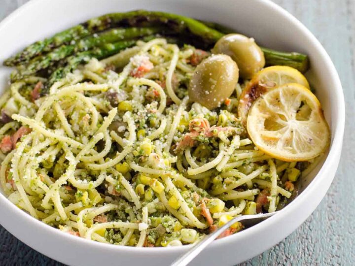 salmon pasta with pesto, asparagus, corn, and olives in a bowl with a fork