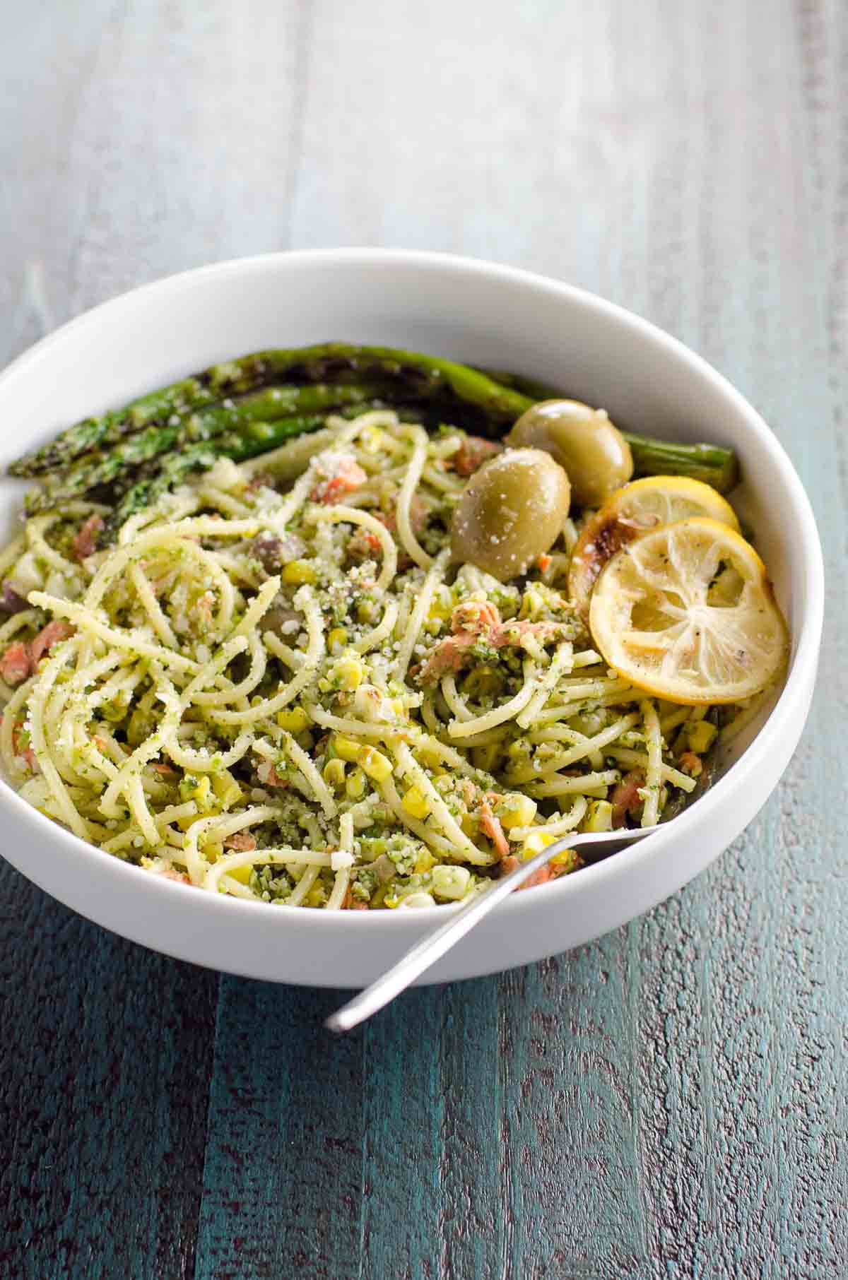 salmon pasta with pesto, asparagus, corn, and olives in a bowl with a fork