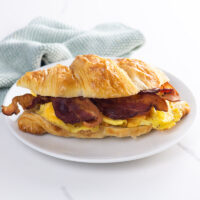 a bacon egg and cheese croissant on a plate with a napkin