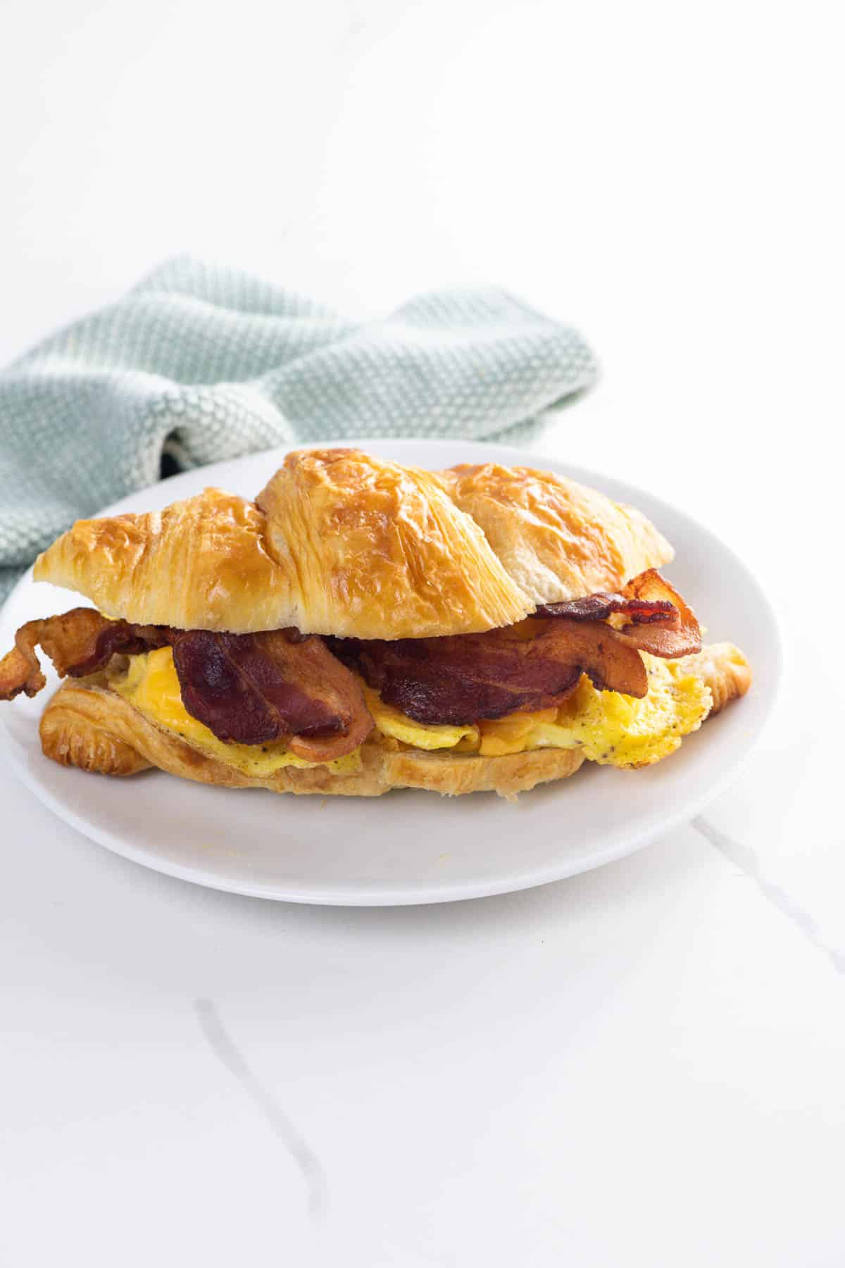 a bacon egg and cheese croissant on a plate with a napkin