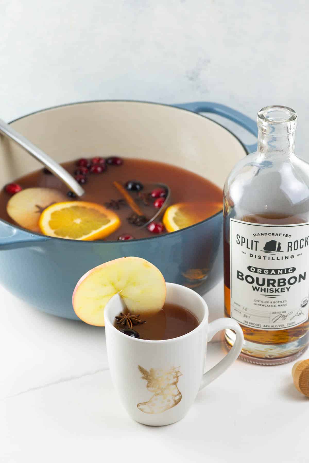 wassail in a mug and pot with a bottle of bourbon