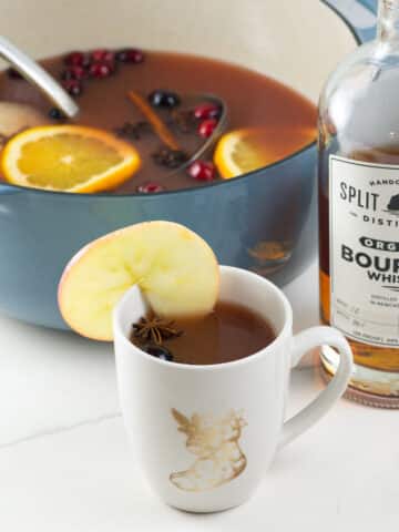 old fashioned wassail recipe in a mug and pot with a bottle of bourbon