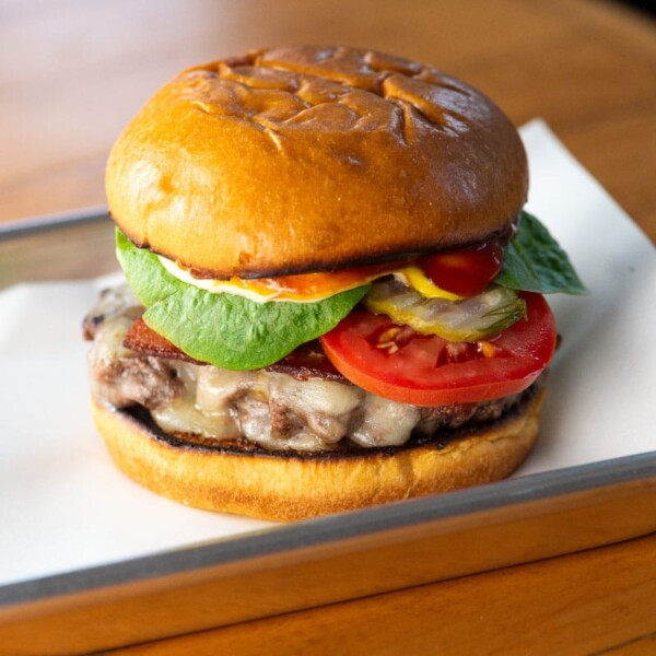 a bacon cheddar burger with lettuce, tomato, ketchup, mustard, and kewpie mayo on a brioche bun