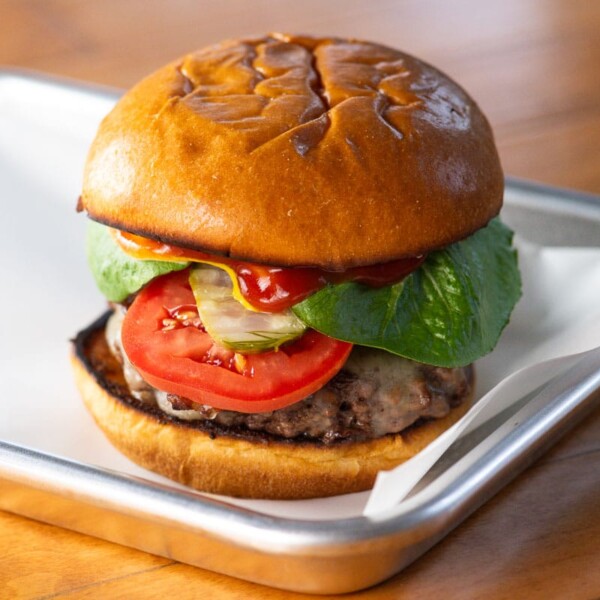 a cheddar burger with lettuce, tomato, pickles, ketchup, mustard, and kewpie mayo on a brioche bun