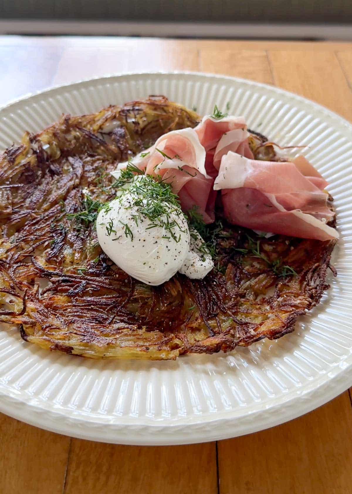 a potato galette on a plate with a poached egg and prosciutto on top