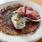 a potato galette on a plate with a poached egg and prosciutto on top