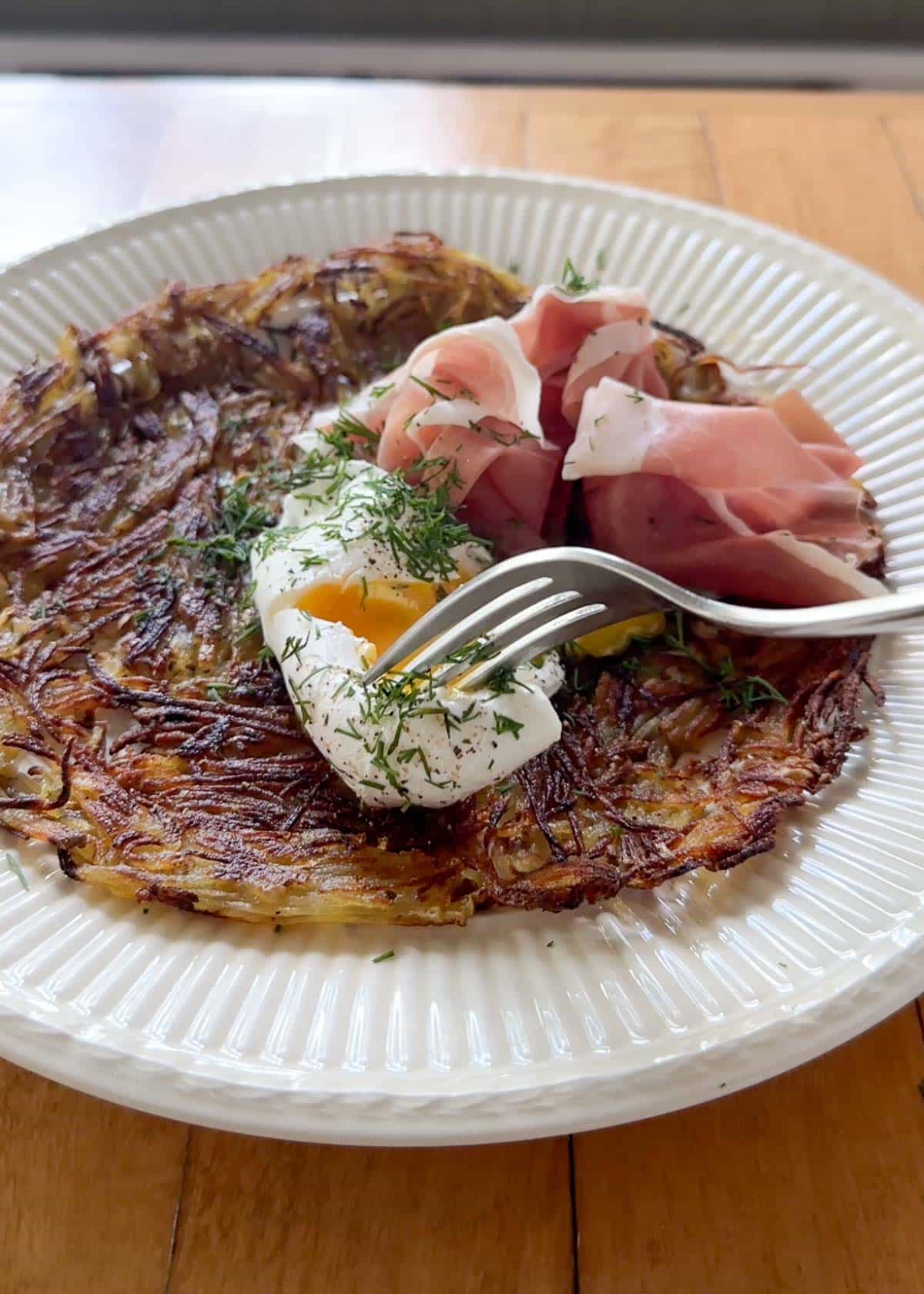 a potato galette on a plate with a poached egg and prosciutto on top 