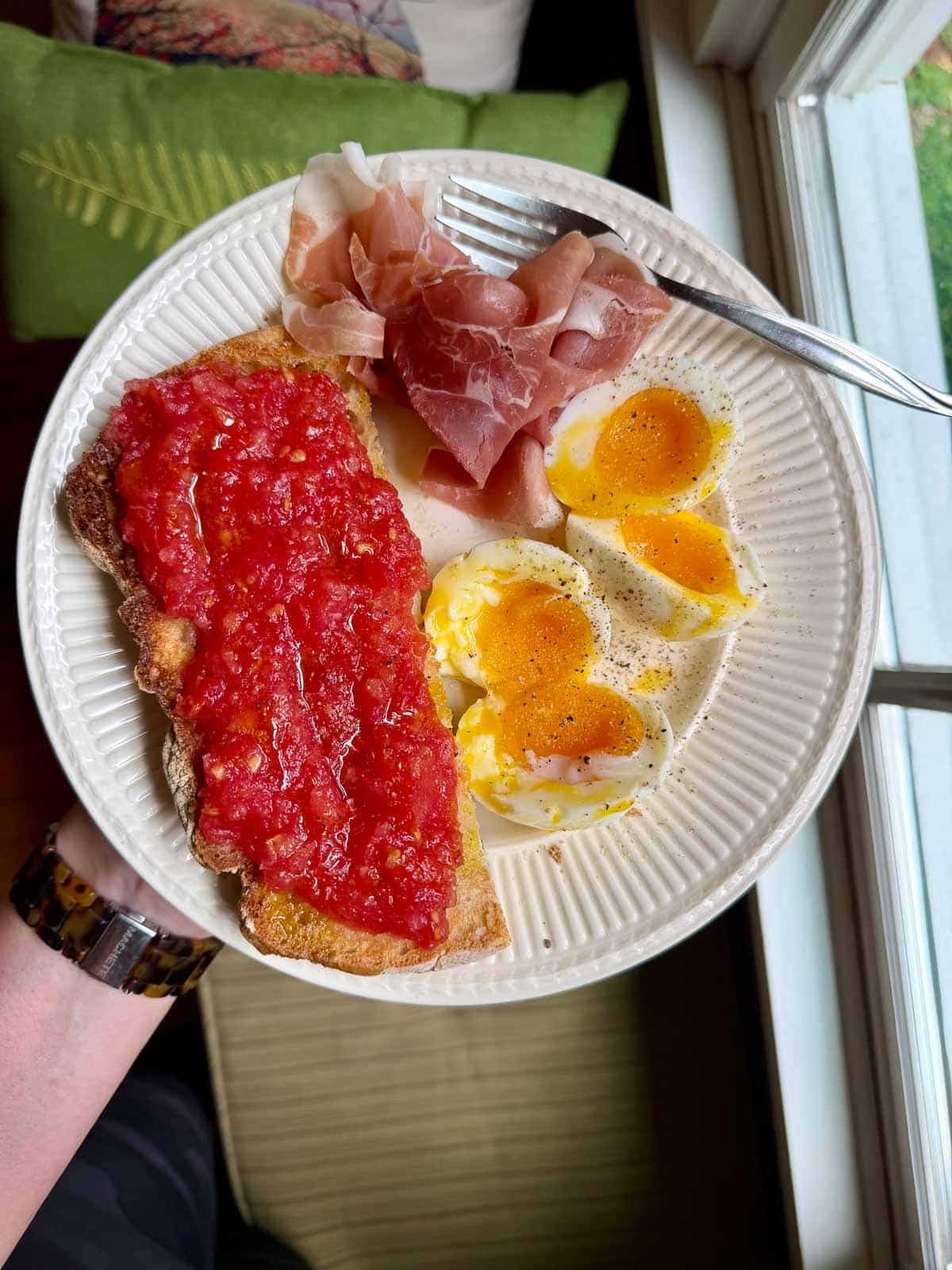 Spanish tomato bread on a plate with two jammy eggs and prosciutto